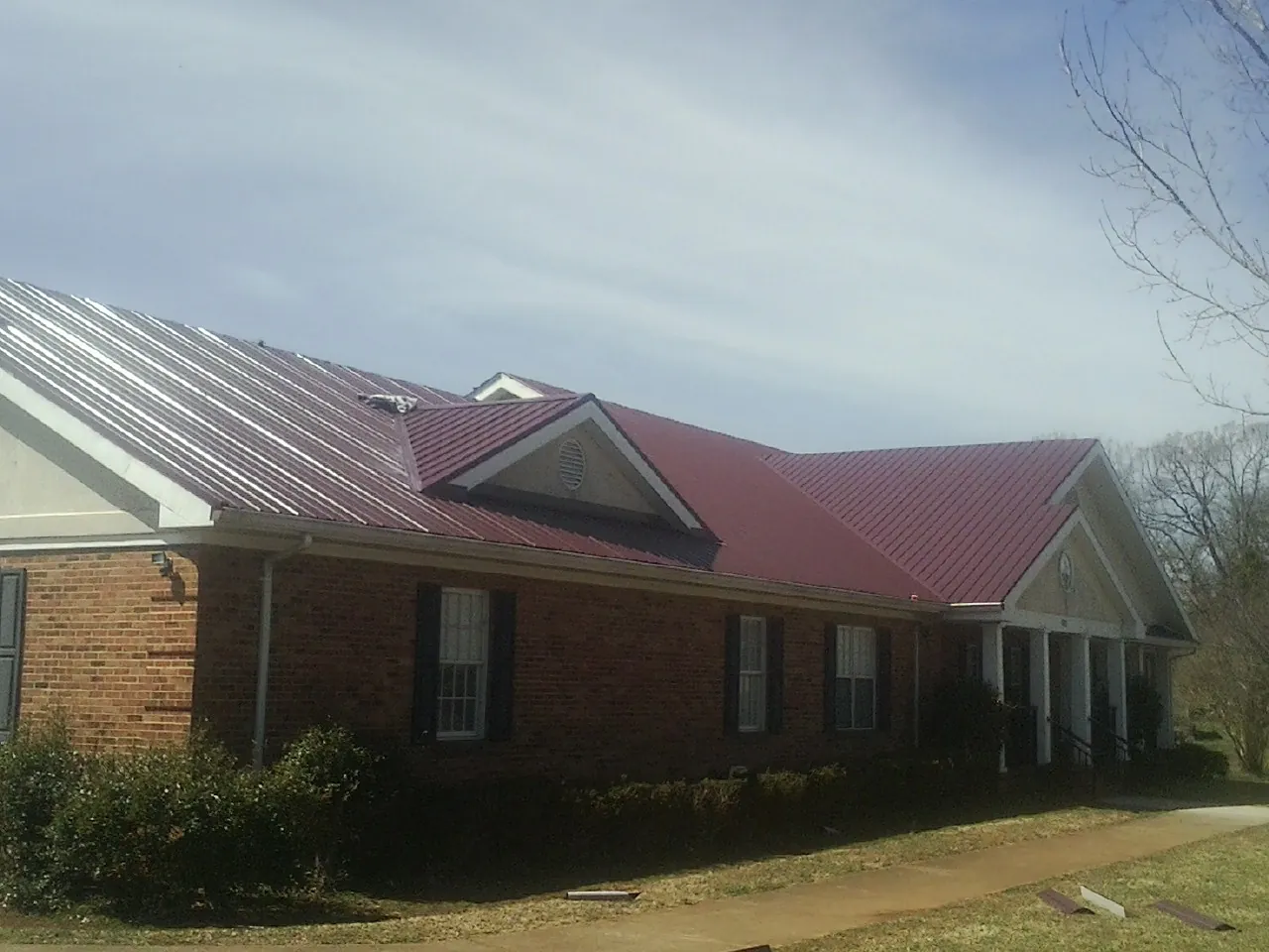 Red metal roof with gabled entries on a long brick building, from a Hail Damage Roof Repair job in Vacaville