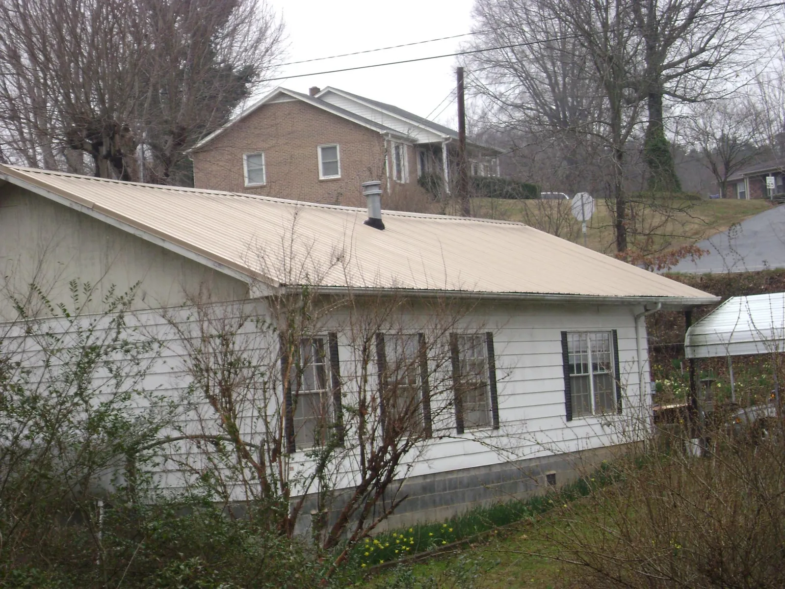 Tan metal roof on a white sided house set into a hillside — Commercial Roofing by Roofing Brothers in Vacaville